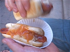 Zwei Hot Dogs von Grays Papaya in einer Hand und die nimmt einen Hot Dog um zu essen.